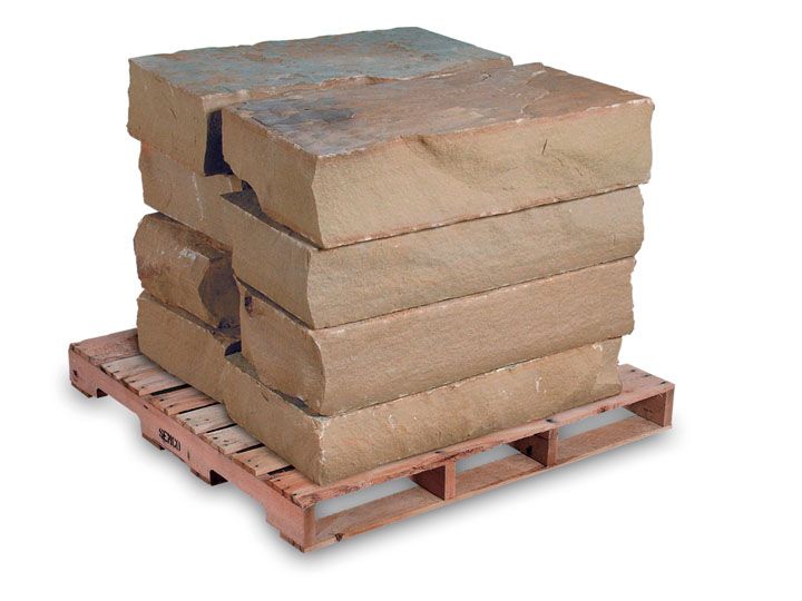 A stack of four large, rectangular tan sandstone blocks sitting on a wooden shipping pallet against a white background.