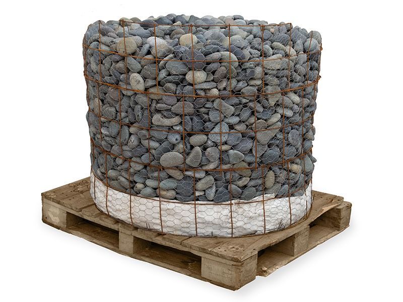 Large cylindrical wire basket filled with gray pebbles on a wooden pallet