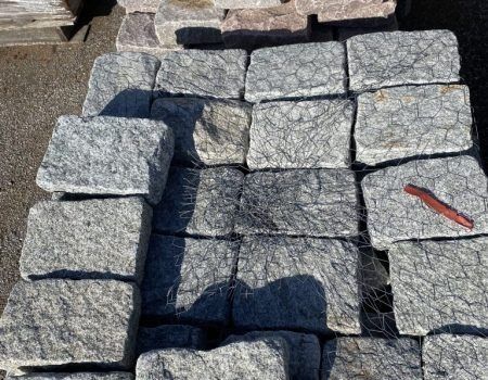 Stacked gray stone pavers on a ground surface, with a small red tool on the right.
