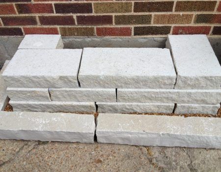 Stacked white stone blocks and pavers arranged in layers against a brick wall.