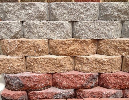 Stacked gray, tan, and reddish stone blocks forming a textured retaining wall pattern.