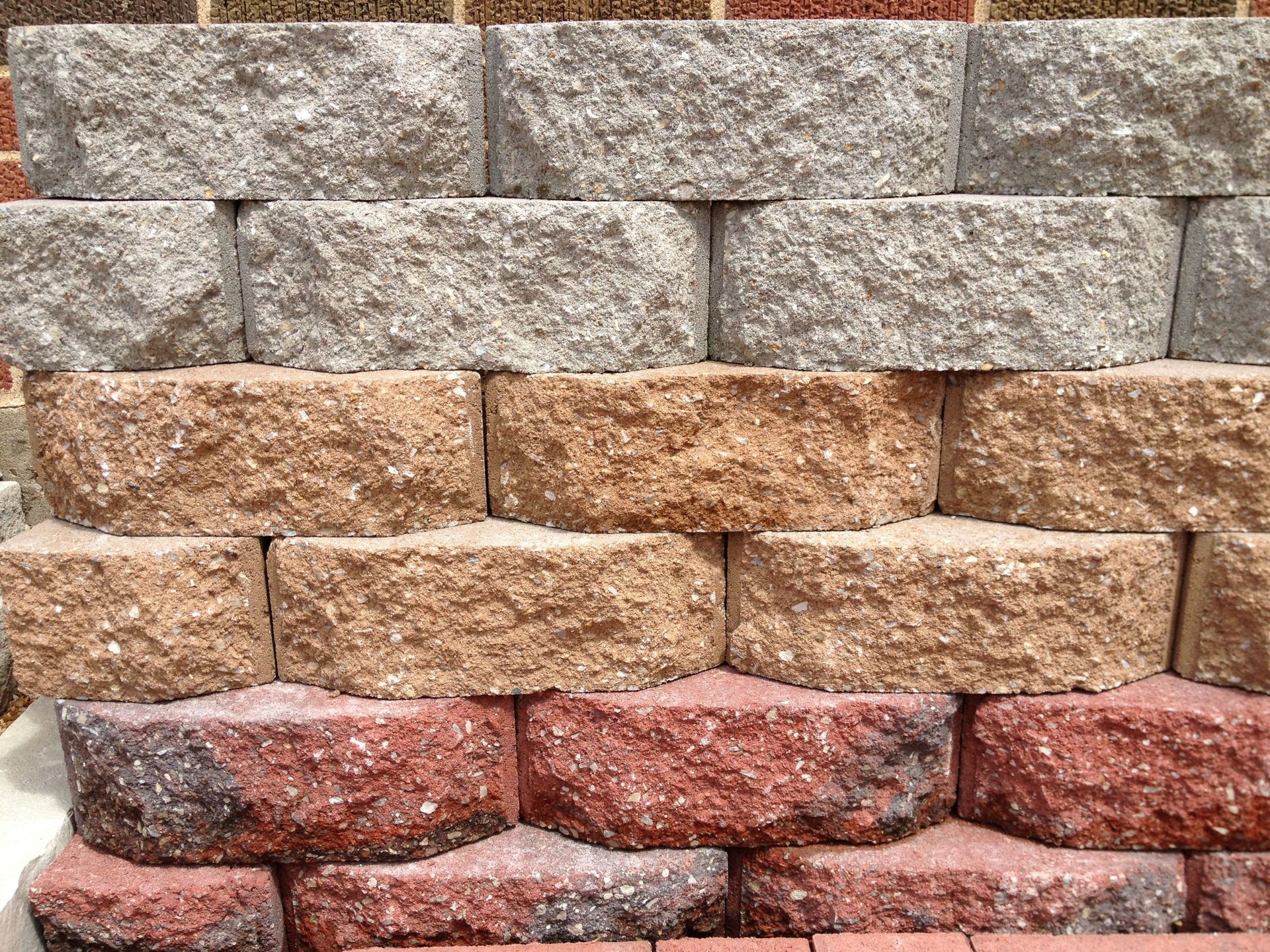 Stacked gray, tan, and red stone retaining wall blocks arranged in rows