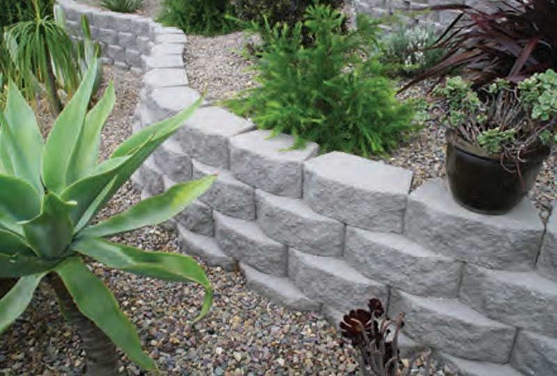 Curved stone retaining wall beside a garden path with succulents and potted plants