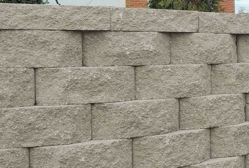 Gray stacked stone wall with a brick building peeking over the top