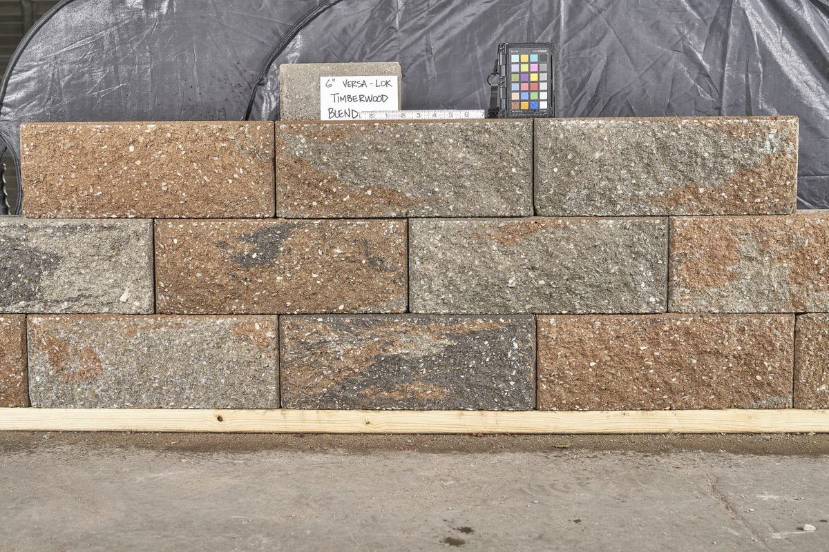 Stacked tan and gray stone retaining wall blocks in front of a black backdrop, with small sample cards on top.