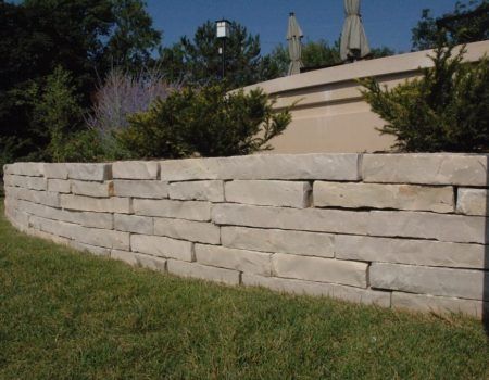 Low stone retaining wall beside green grass and shrubs under a sunny sky