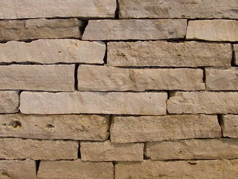 Close-up of stacked beige stone bricks forming a rough wall pattern