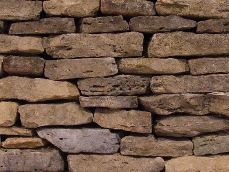 Stacked tan and gray stone wall with rough, uneven stones