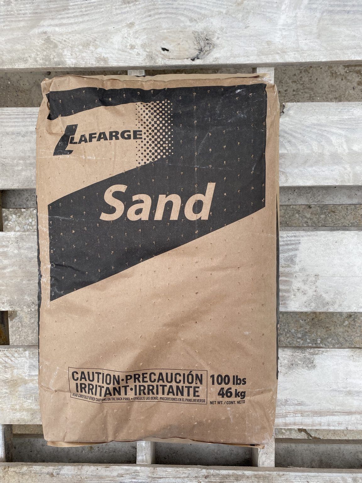 Lafarge sand bag leaning against stacked concrete blocks, with black and tan packaging.