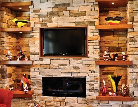 Stone fireplace wall with two TVs and built-in shelves holding colorful decor pieces