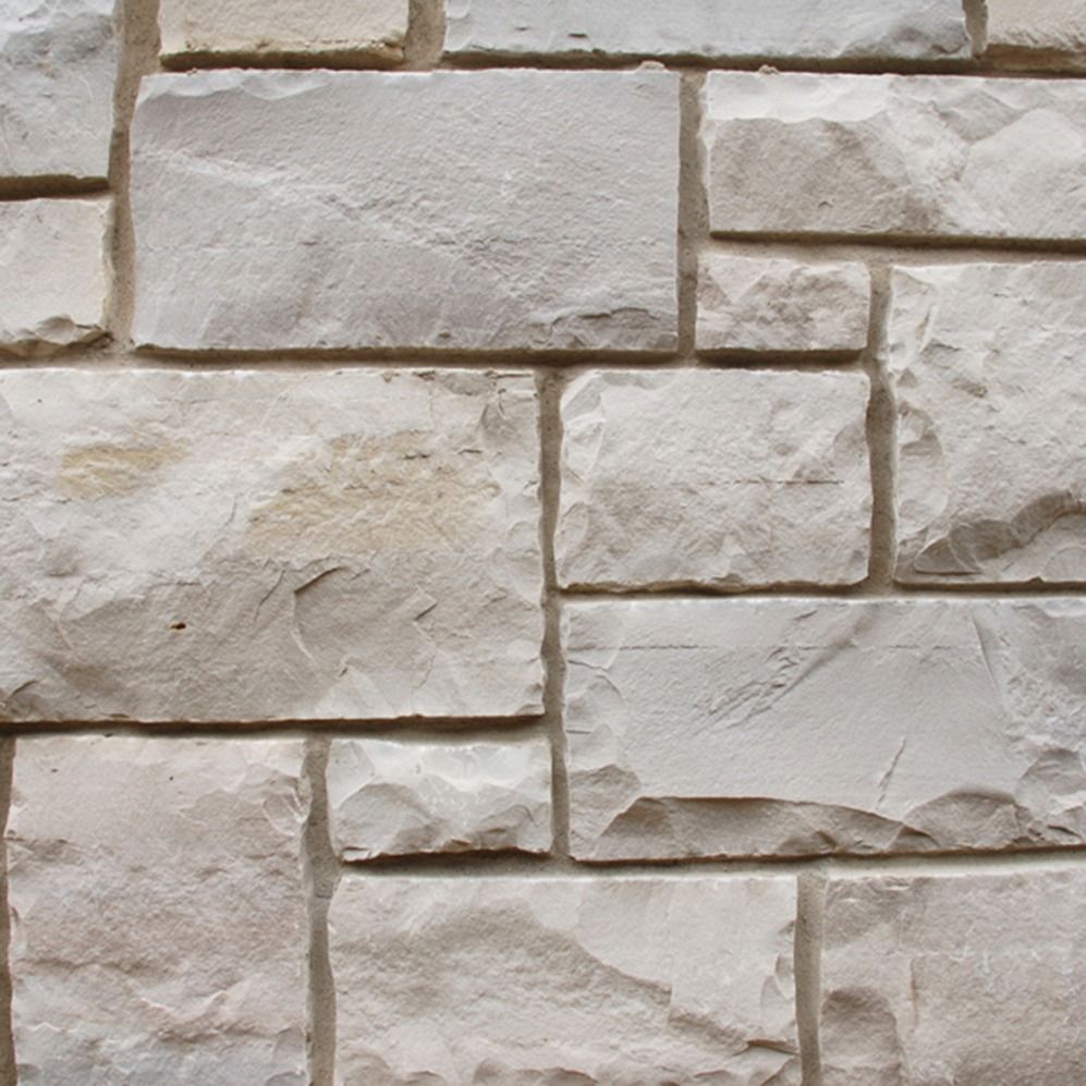Close-up of beige stacked stone wall with rough, textured blocks and mortar lines