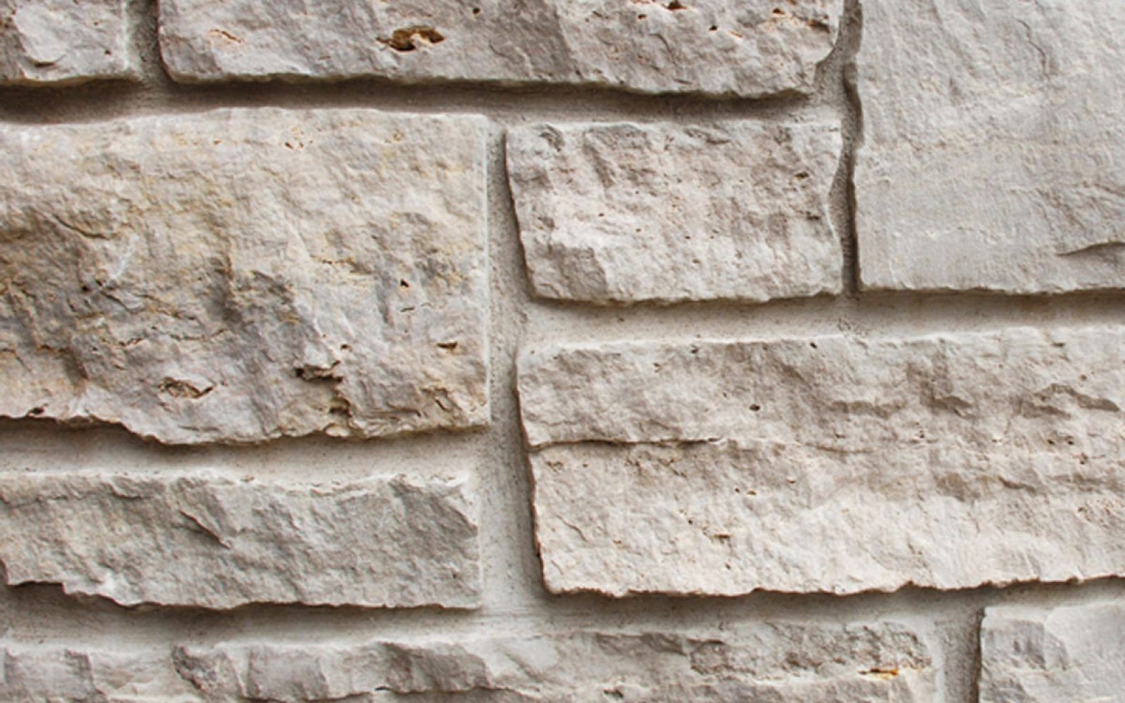 Close-up of beige stone wall with rough, stacked masonry blocks and light mortar lines