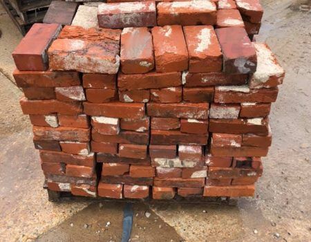 Stack of worn red bricks on a pallet outdoors, with some white mortar residue.