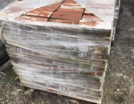 Shrink-wrapped pallet of red bricks on gravel ground