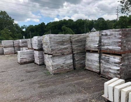 Stacks of shrink-wrapped bricks or pavers on pallets in an outdoor yard under cloudy skies