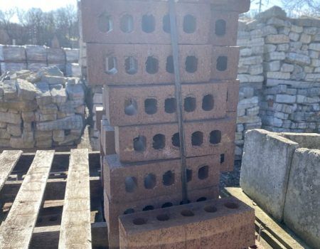 Stacked cinder blocks on wooden pallets in an outdoor yard beside stone walls.