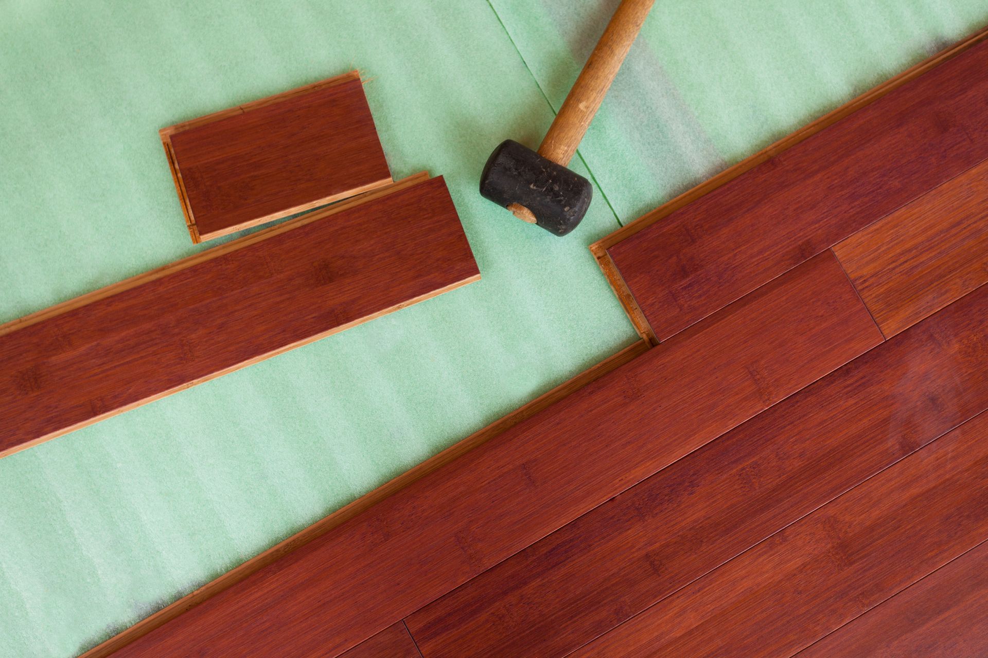 Installing hardwood flooring: hammer and planks on green underlayment.