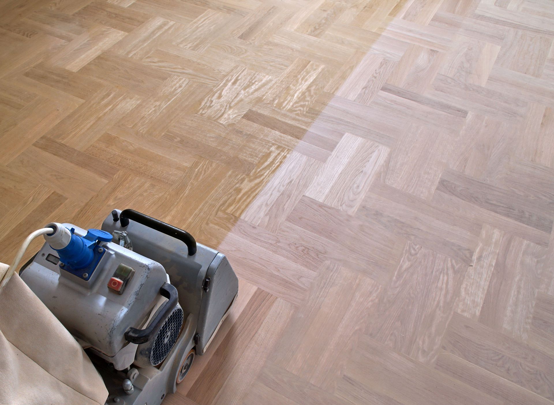 Floor sander on a herringbone patterned hardwood floor, sanding the wood.