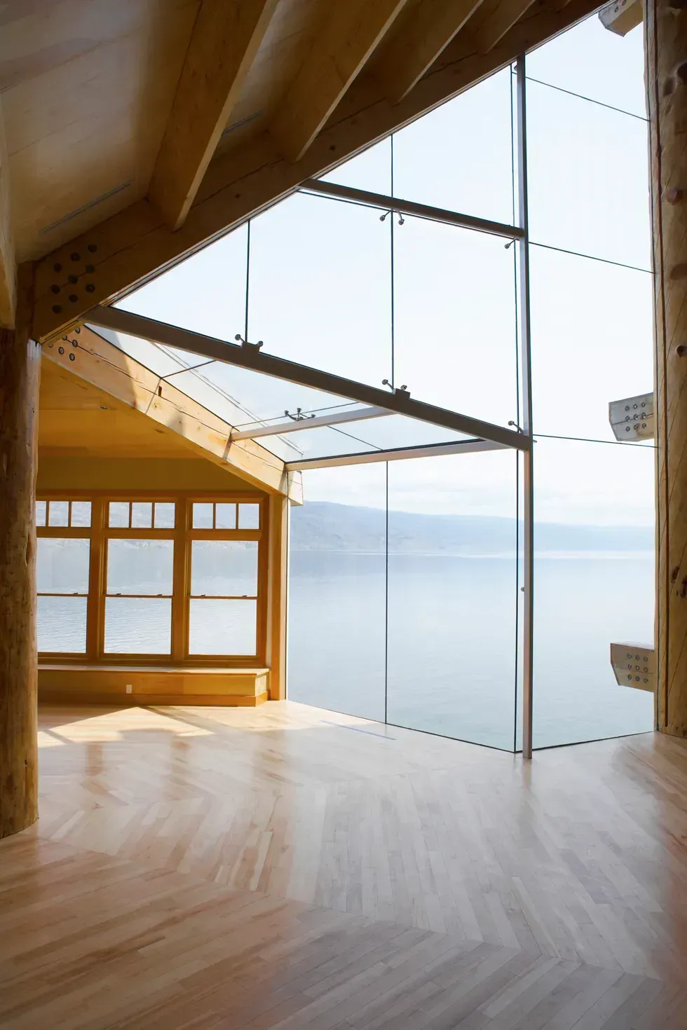Interior of a wood-framed building with large glass windows overlooking a body of water.