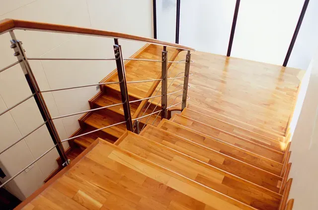 Wooden staircase with stainless steel handrail, ascending from bottom left corner to top right landing.