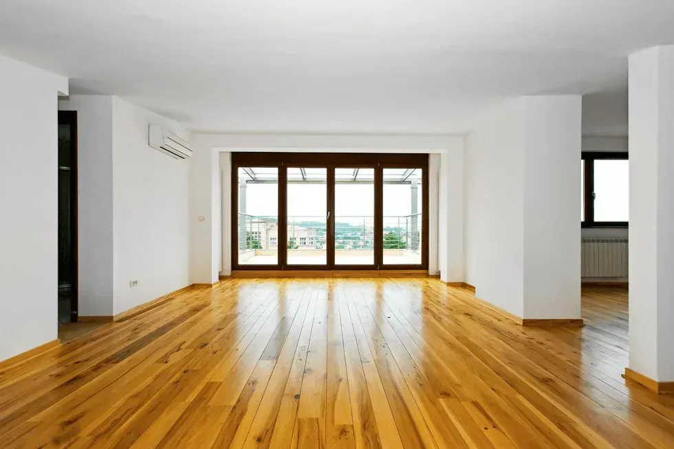 Empty room with wooden floor, white walls, and glass doors opening to a balcony.