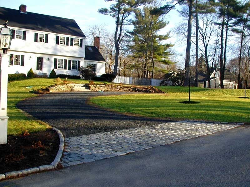 A white colonial-style house sits behind a curving gravel driveway featuring a cobblestone apron.