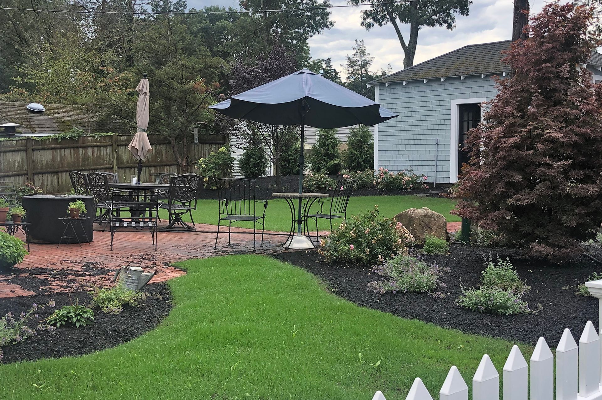 A tiered stone retaining wall separates a vibrant, multi-level garden with colorful shrubs and groundcover from a lawn.