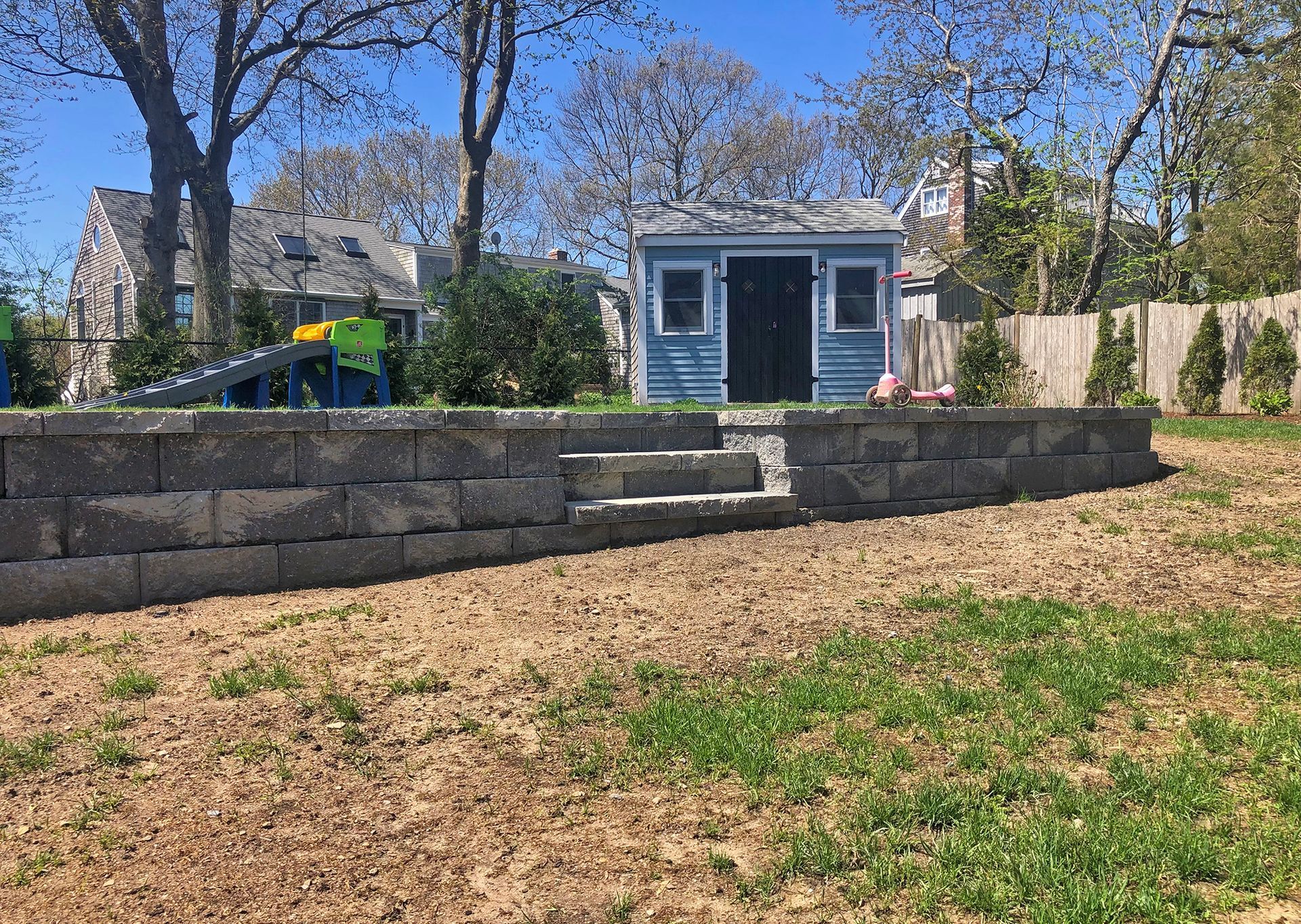 A stonemason lays stones into a mortar bed on a partial garden wall in an outdoor setting.