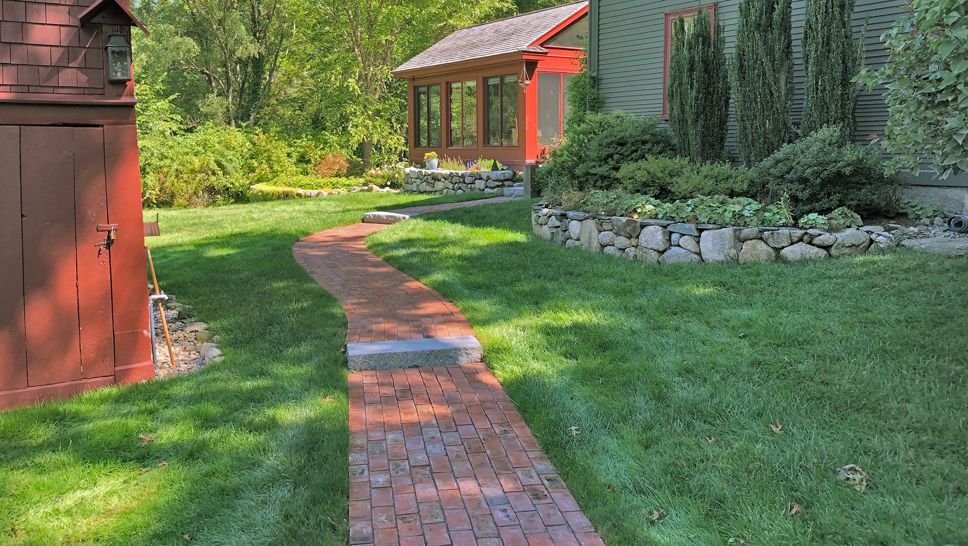 Grey stone pavers being laid on a gravel path, with a level and tools nearby, leading toward a house entrance.