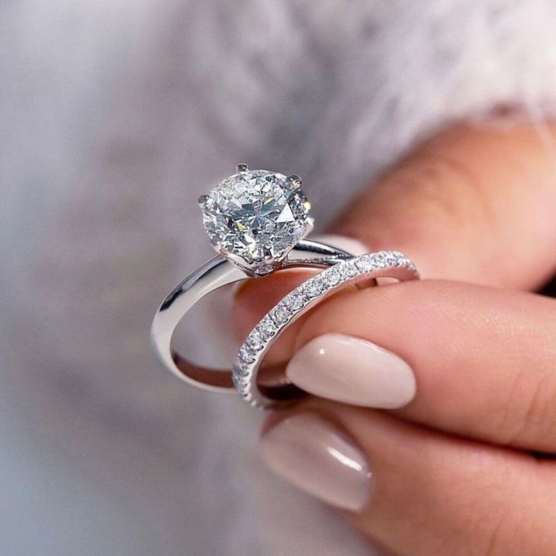 Person holding two diamond rings, engagement ring with solitaire and band with small diamonds.