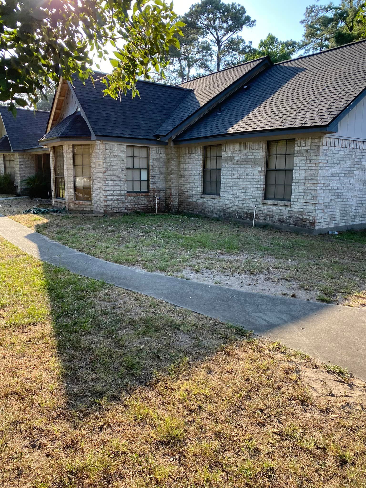 A brick house with a black roof and a sidewalk in front of it.