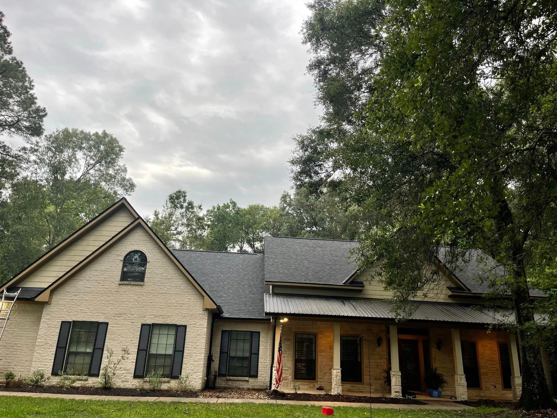 A large white brick house with a black roof is surrounded by trees.