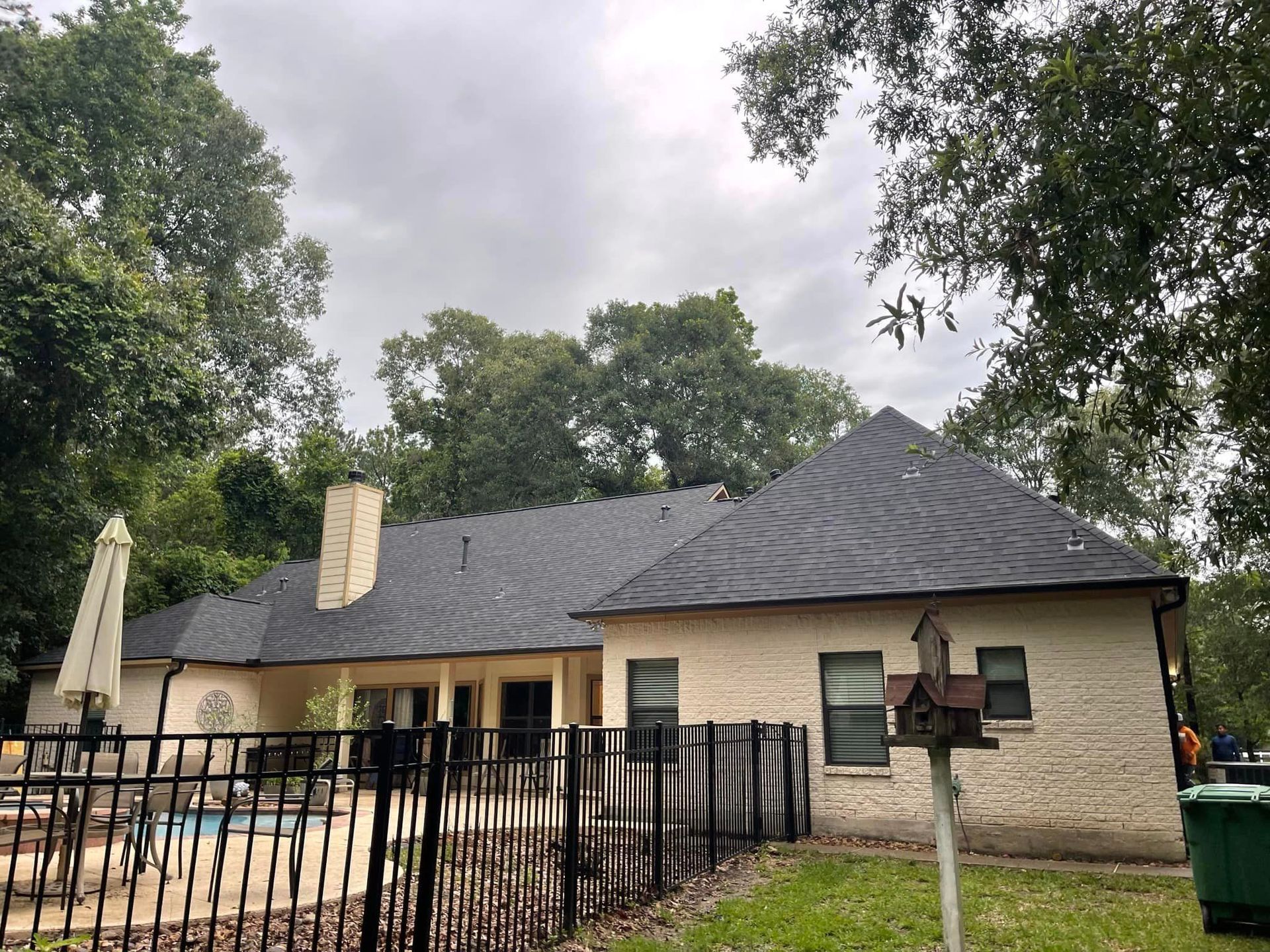 A white brick house with a black roof and a fence around it.