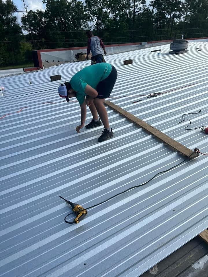 A man is working on a metal roof with a drill.