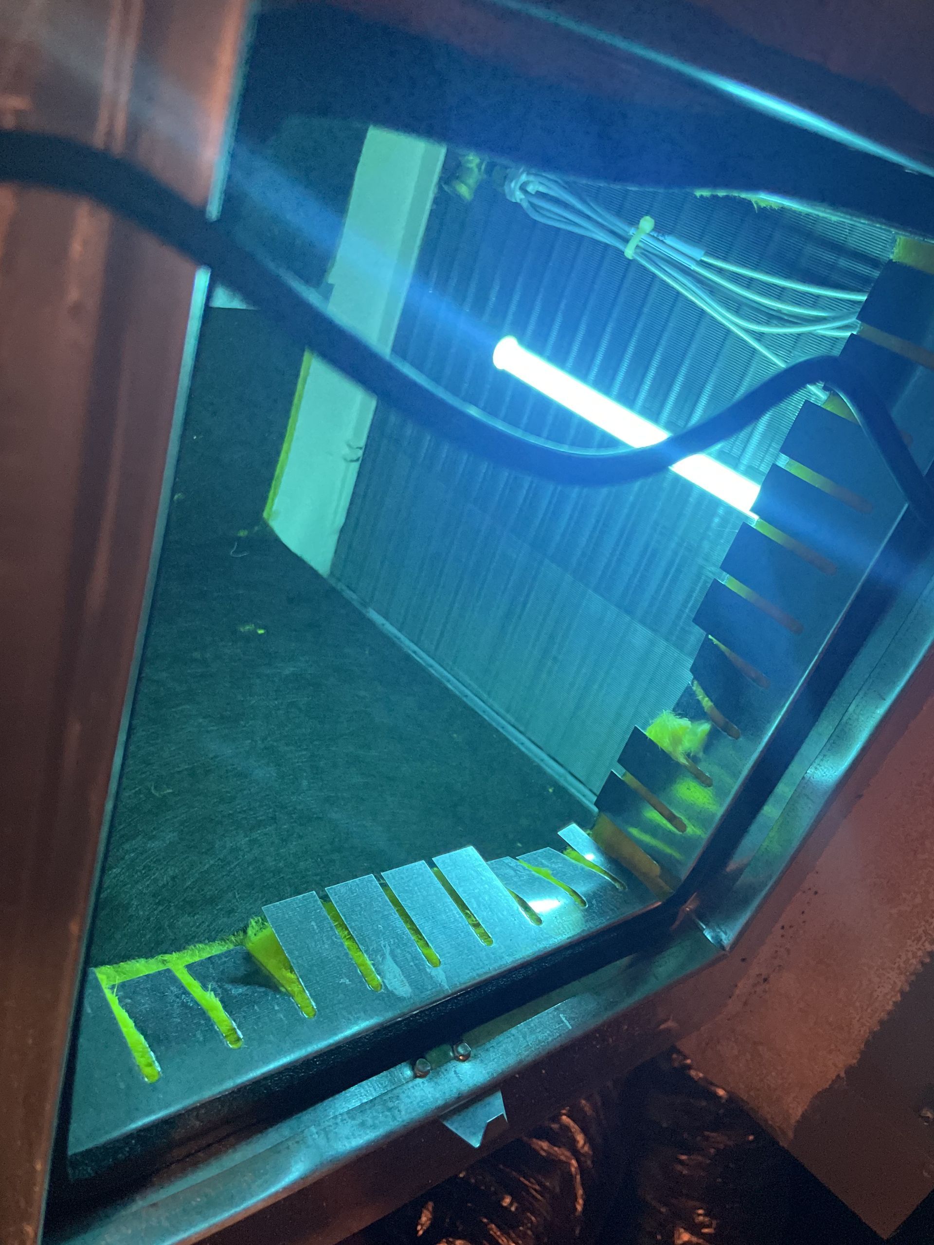 Blue UV light inside an air conditioning unit, illuminating cooling coils and internal components.