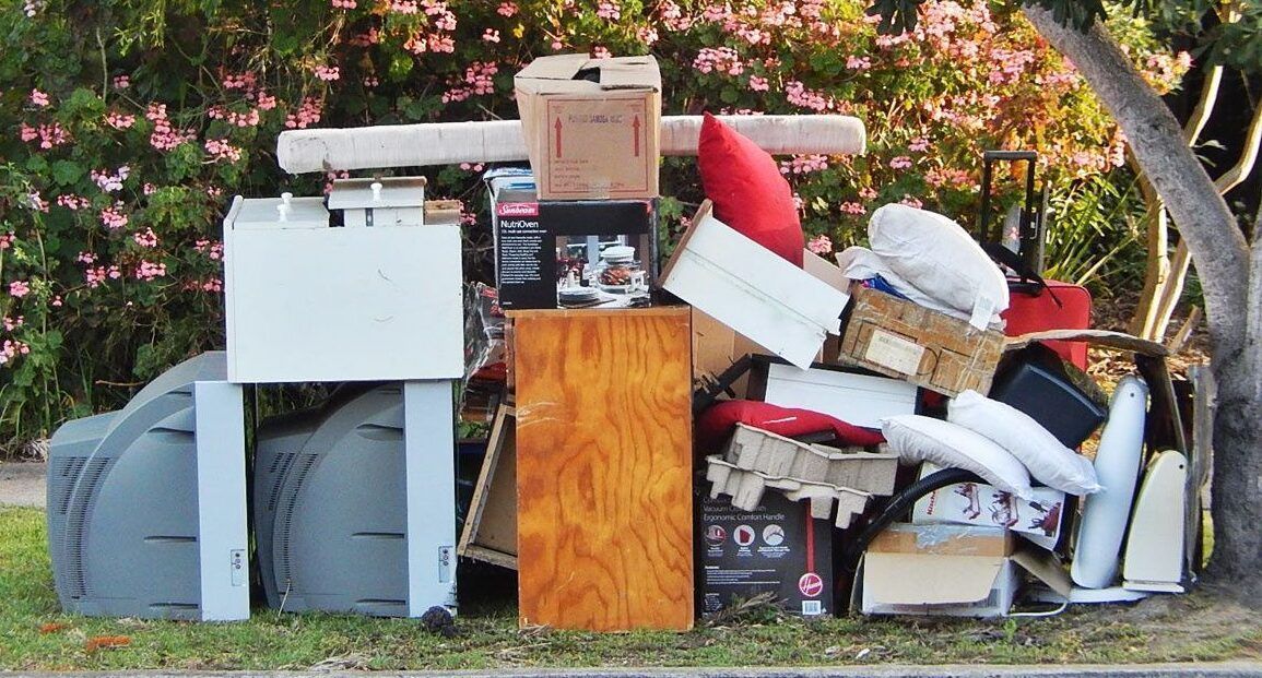 Pile of discarded items, including cardboard boxes, furniture, and a mailbox, on a lawn.