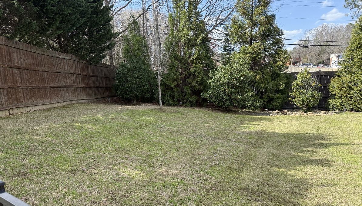 Lush green lawn with colorful flower beds in front of a white house with a porch and garage.