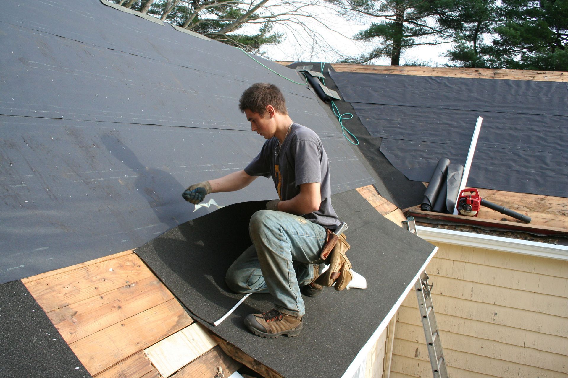 A person kneels on a roof, applying sealant during a roofing project.