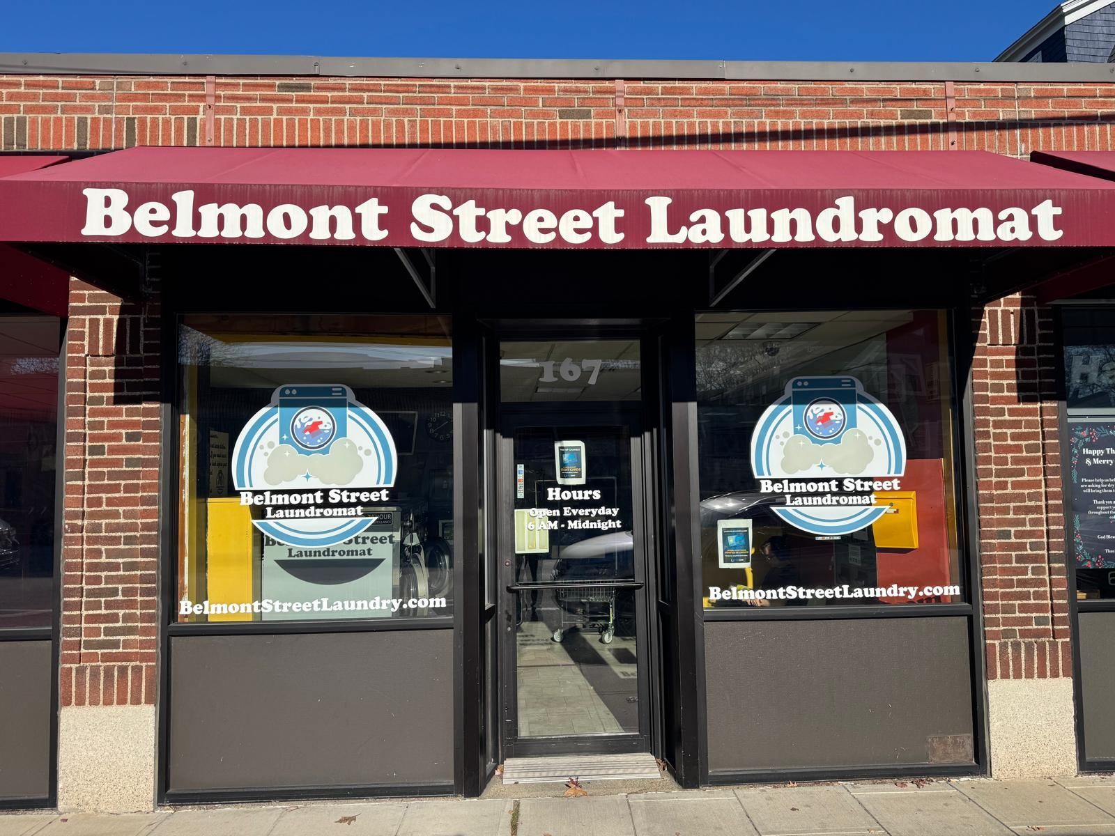 Belmont Street Laundromat storefront with a red awning. The entrance is a glass door with signage.