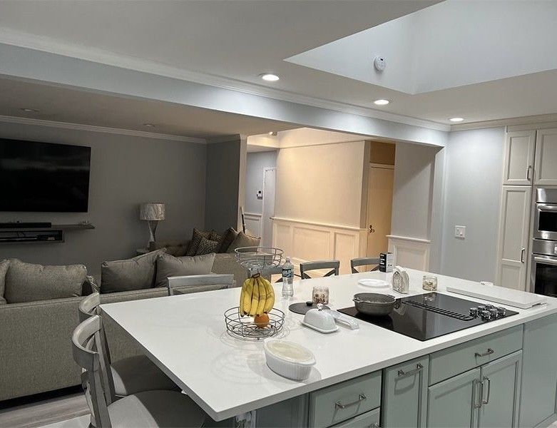 Modern open-plan kitchen with white island, gray sofa, wall TV, and built-in cabinets under recessed lighting