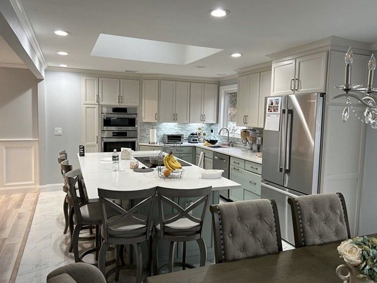 Bright modern kitchen with white cabinets, stainless appliances, island, and gray dining chairs