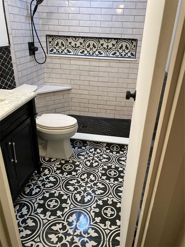 Small bathroom with black-and-white patterned floor, white subway tile, toilet, sink, and shower area.