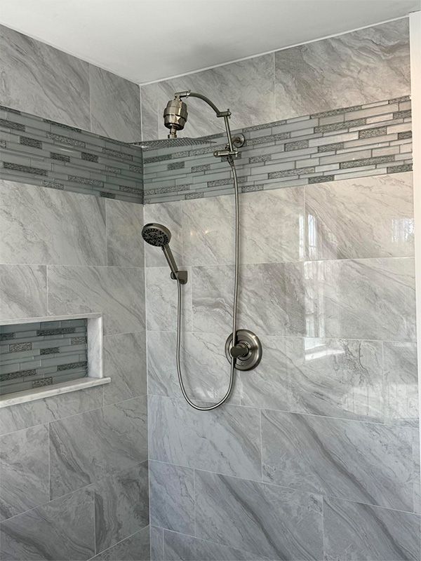 Walk-in shower with marble-look tile, mosaic border, and handheld showerhead nearby