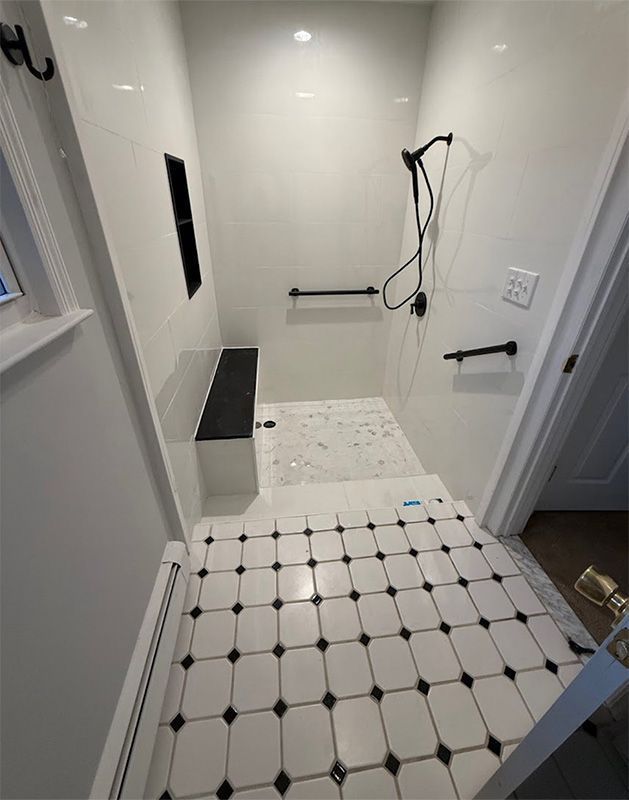 Empty white tiled bathroom under renovation with shower area, grab bars, and a bench