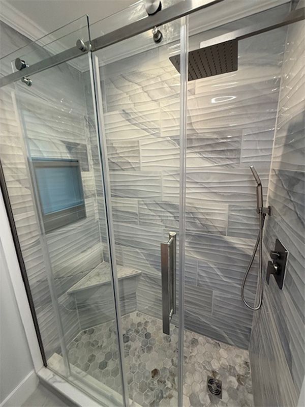 Glass-enclosed modern shower with marble walls, built-in shelf, and pebble floor drain.