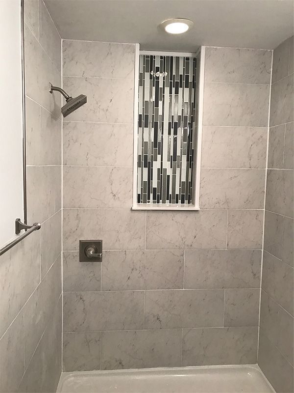 Tiled shower with chrome showerhead, wall niche, and recessed ceiling light