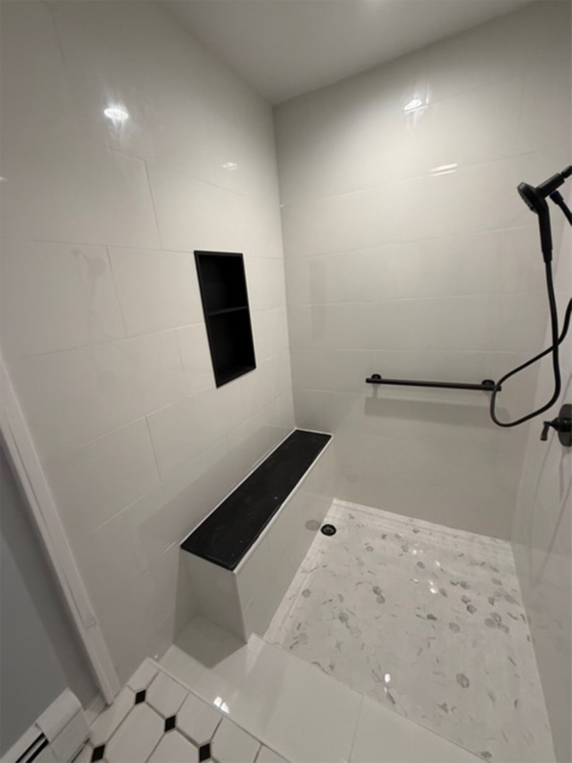 Modern white tiled shower with black bench and recessed shelf, handheld showerhead on the right.