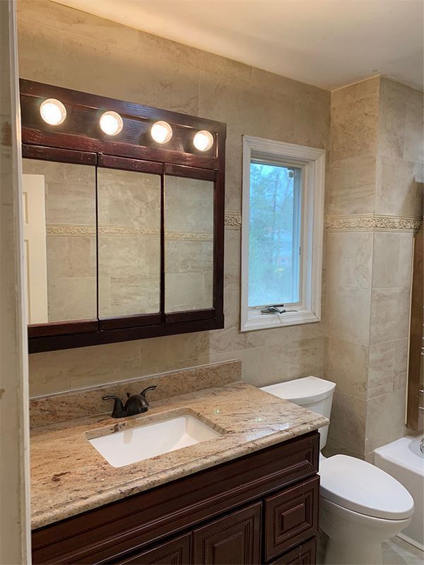 Bathroom with dark wood vanity, granite countertop, three-light mirror, and toilet beside a tiled shower.