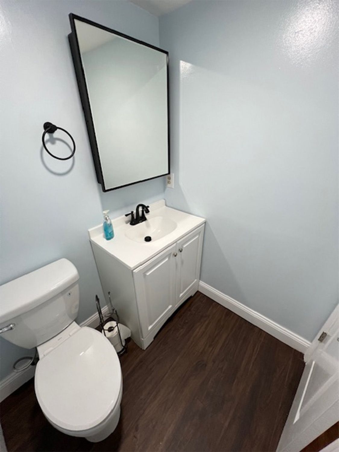 Small bathroom with toilet, vanity sink, mirror, and dark wood floor on light gray walls.