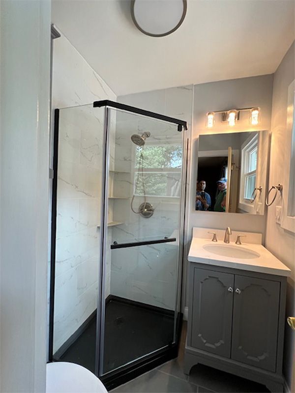 Modern bathroom with glass shower, gray vanity, mirror lights, and white tile floor